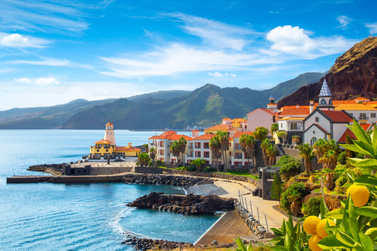 Blick auf eine Bucht auf Madeira, links das Meer, rechts H&auml;user und Berge, gr&uuml;n bewachsen